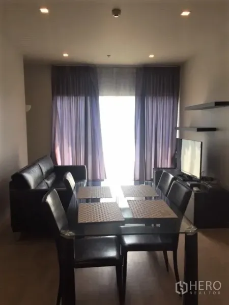 Condominium for rent in Bangkok - Open-plan living and dining area with glass table, black leather sofa, TV console and floor-to-ceiling curtains in a 2-bedroom condo near BTS Phrom Phong.