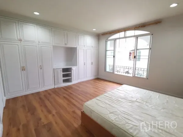 Townhouse for rent in Yan Nawa, Bangkok - Spacious master bedroom with wall-to-wall white wardrobes, wood flooring and a wide window.