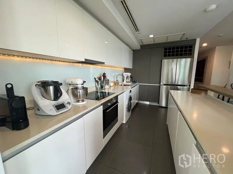 Condominium for sale in Khlong San, Bangkok - Galley kitchen with island counter, full-height fridge, and countertop appliances.