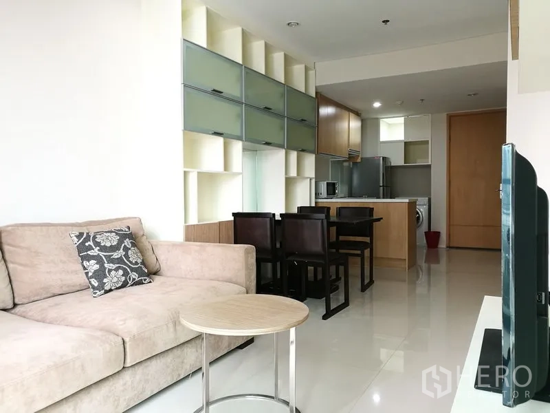 Condominium for rent in Ratchathewi, Bangkok - Open‑plan lounge with sofa, dining set and wall storage leading to a fitted kitchen.