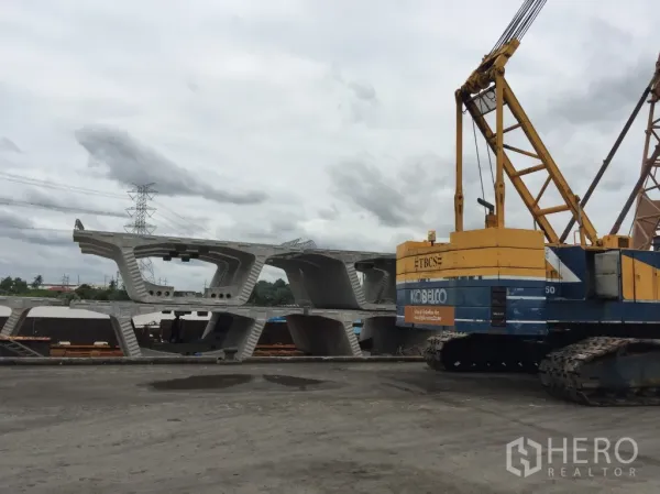 Warehouse for rent in Pathum Thani - Open industrial yard with crawler crane and stacked precast concrete beams at a warehouse site in Mueang Pathum Thani.