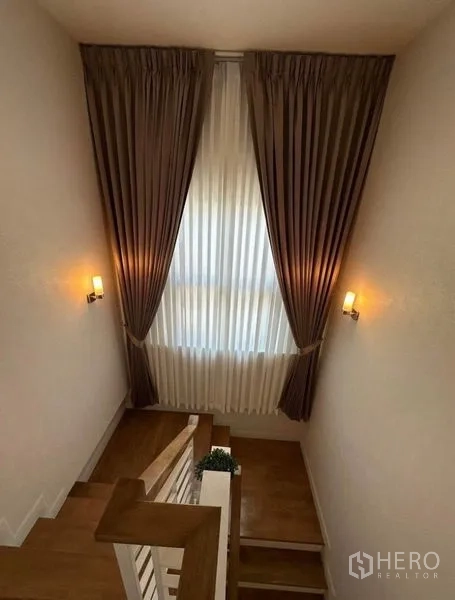 Detached House for rent - Staircase landing with warm wall sconces and tall curtains over a picture window.