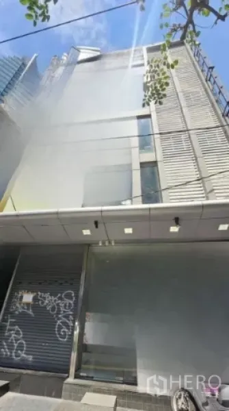 Retail Space for rent in Watthana, Bangkok - Mid-rise commercial building exterior with metal façade and closed roller shutters under a canopy on a sunny day in Bangkok.