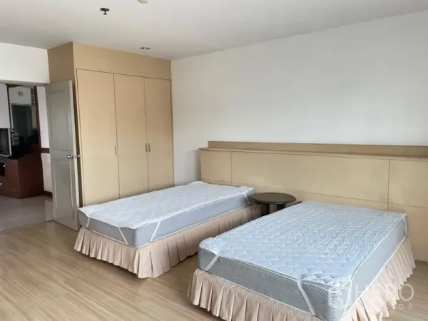 Condominium for rent in Khlong Toei, Bangkok - Spacious twin-bed room with built-in wardrobe, wood floors, and neutral walls.