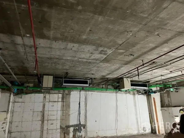 Retail Space for rent - Close-up of industrial ceiling showing exposed HVAC units, green piping and fire sprinkler lines in a raw retail shell.