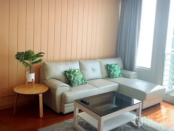 Condominium for rent in Khlong Toei, Bangkok - Cozy living room with L-shaped sofa, glass coffee table and balcony door.