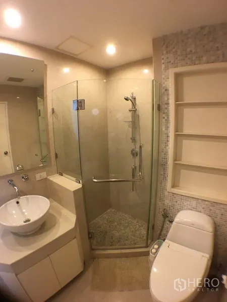 Condominium for rent in Khlong Toei, Bangkok - Modern bathroom with glass-enclosed shower, vanity basin and toilet.