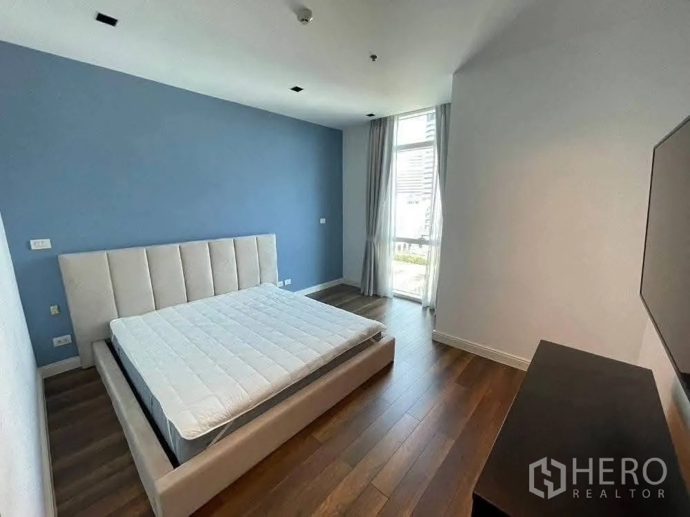 公寓 for rent in Pathum Wan, Bangkok - 卧室配软包床与木地板，落地窗可见城市景观。