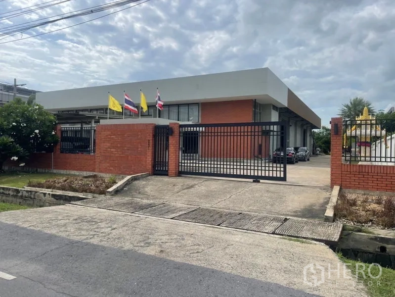 Factory for rent in Mueang Samut Prakan, Samut Prakan - Gated brick-facade factory with wide driveway and flags in Phraeksa