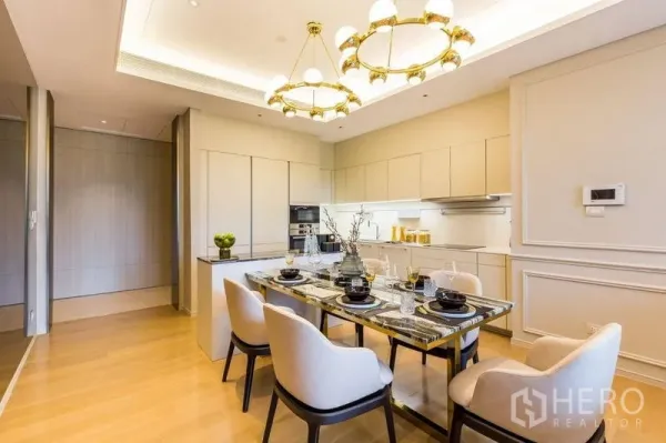 Condominium for rent in Pathum Wan, Bangkok - Elegant dining space with marble table under gold chandeliers beside a modern white kitchen.