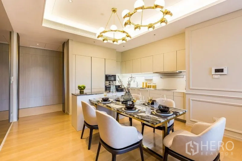 Condominium for rent in Pathum Wan, Bangkok - Elegant dining space with marble table under gold chandeliers beside a modern white kitchen.