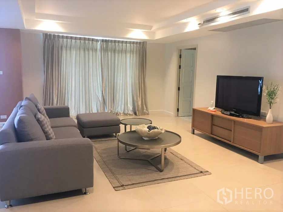 公寓 出租在Watthana, Bangkok - 明亮客厅，电视柜、大窗帘、灰色沙发与圆形茶几铺设地毯。
