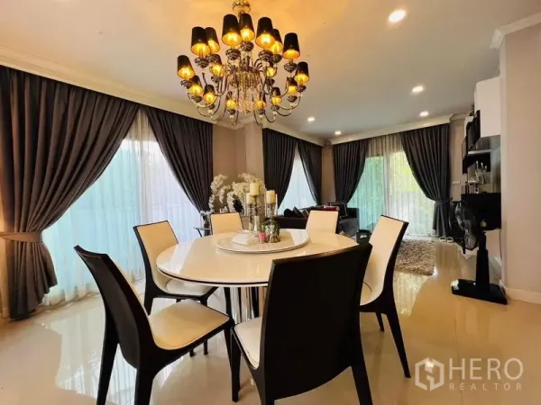Detached House for rent or sale in Bang Khen, Bangkok - Round dining table under an ornate chandelier with floor-to-ceiling drapes and warm lighting.