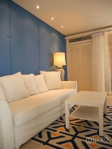 Condominium for rent in Khlong Toei, Bangkok - Sitting area with white couch, blue wall panels and sheer curtains.