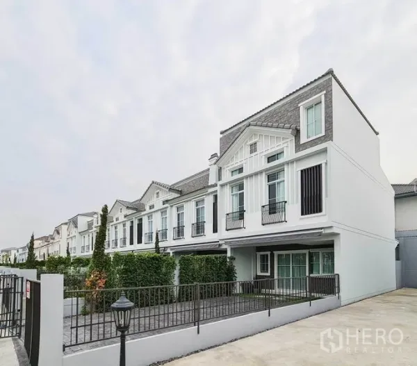 Townhouse for rent in Prawet, Bangkok - Modern townhouse row with gabled roof, large windows, gated driveway and front yard.