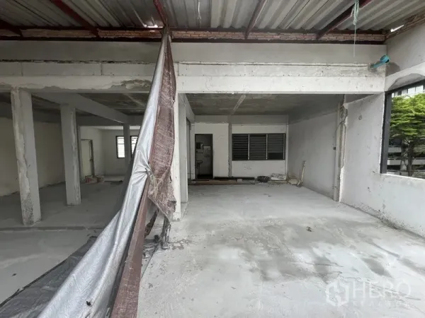 Retail Space for rent in Watthana, Bangkok - Partially covered retail level under renovation with concrete flooring and louvered windows.