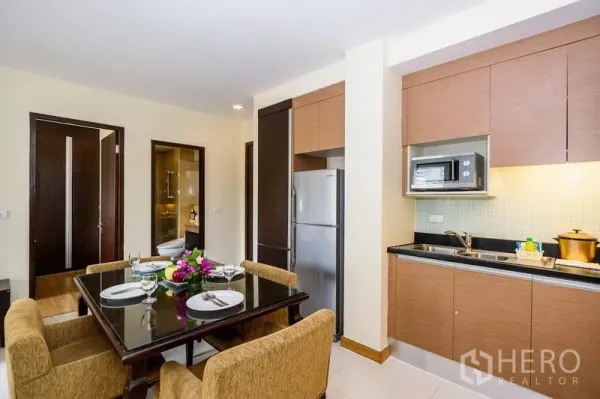 Condominium for rent in Khlong Toei, Bangkok - Compact kitchen with built-in cabinets, microwave and full-size refrigerator beside a four-seat dining table.