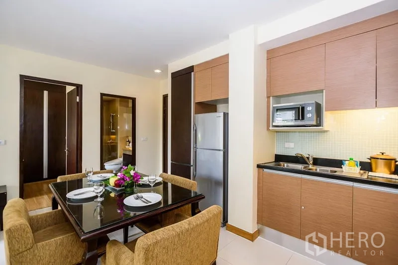 Condominium for rent in Khlong Toei, Bangkok - Compact kitchen with built-in cabinets, microwave and full-size refrigerator beside a four-seat dining table.