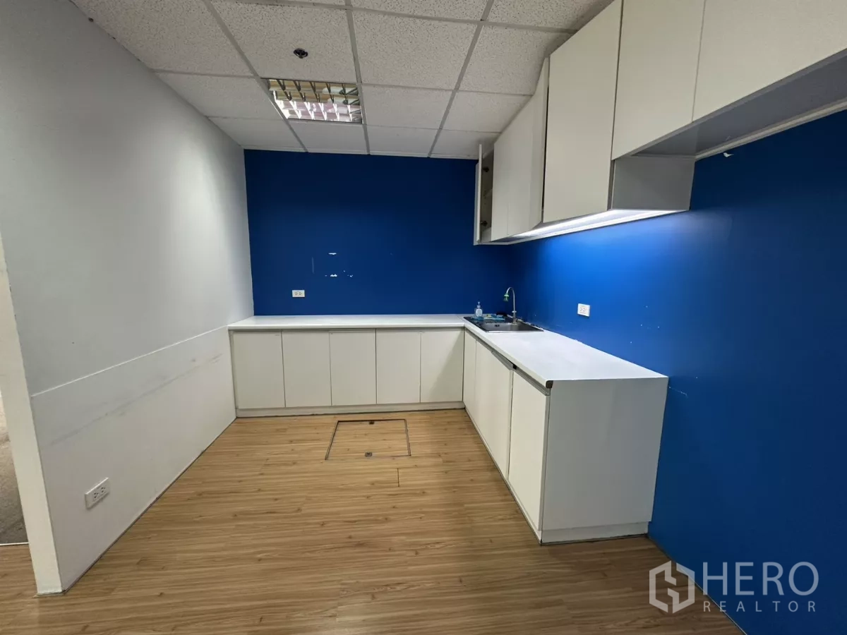 Office Space for rent in Watthana, Bangkok - Compact kitchenette with white cabinets, sink and blue backsplash wall.