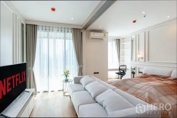 公寓 出租在Ratchathewi, Bangkok - 采光充足的起居与卧室区，落地窗帘、沙发和靠阳台的工作台。