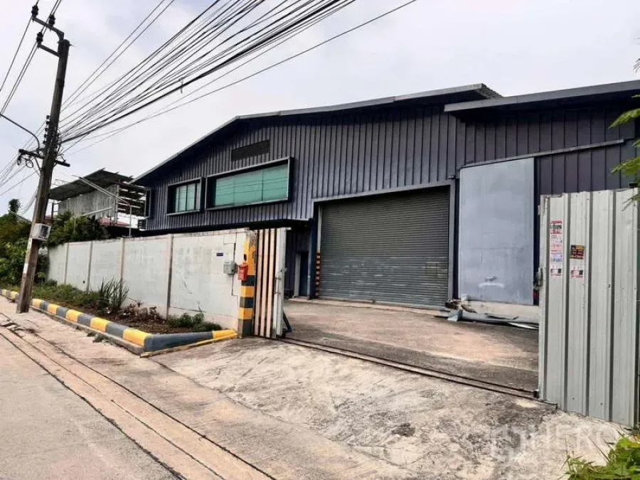 Warehouse for rent in Prawet, Bangkok - Street view of gated industrial warehouse with metal cladding and roller shutter entrance in Prawet.