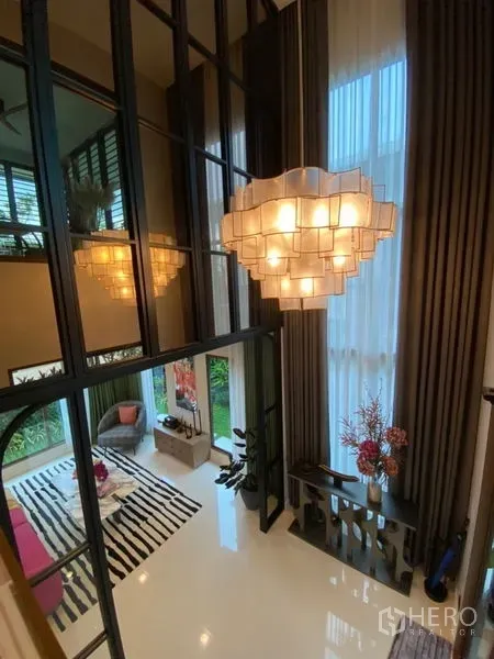 Detached House for sale in Bang Kapi, Bangkok - Double-height living space with statement chandelier, tall curtains and mirror wall.