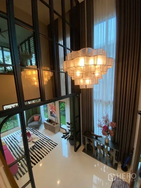 Detached House for sale in Bang Kapi, Bangkok - Double-height living space with statement chandelier, tall curtains and mirror wall.
