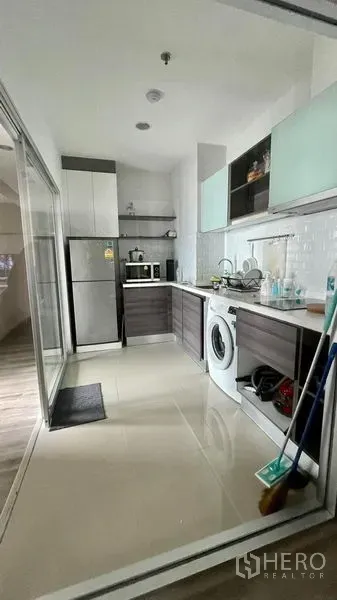 Condominium for sale in Sathon, Bangkok - Enclosed kitchen behind sliding glass with cabinets, fridge, microwave, sink and washing machine on tiled floor.