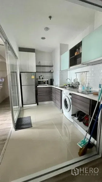 Condominium for sale in Sathon, Bangkok - Enclosed kitchen behind sliding glass with cabinets, fridge, microwave, sink and washing machine on tiled floor.