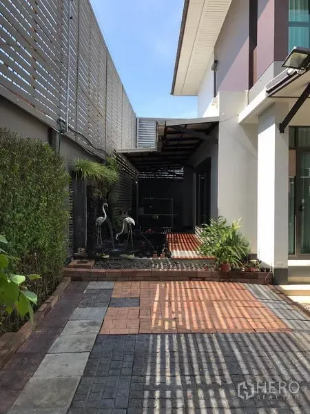 Detached House for rent in Bang Kapi, Bangkok - Side yard with paved patio and decorative pond beside the house, framed by hedges.