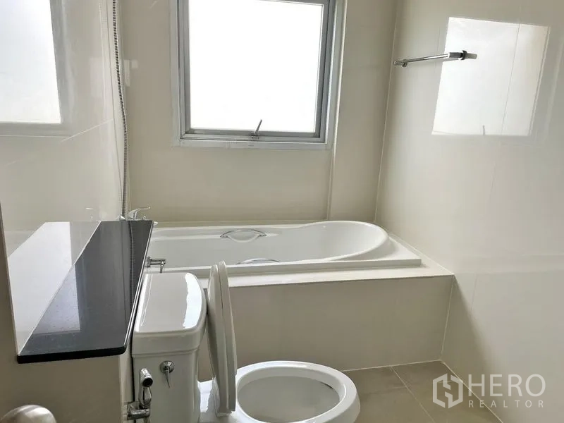 Condominium for rent in Khlong Toei, Bangkok - Clean bathroom with bathtub, shower handset, window and toilet.