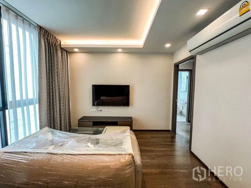 คอนโด ขายในHuai Khwang, Bangkok - ห้องนั่งเล่นสว่าง มีโซฟา ทีวีติดผนัง เครื่องปรับอากาศ และประตูเชื่อมไปยังห้องนอน