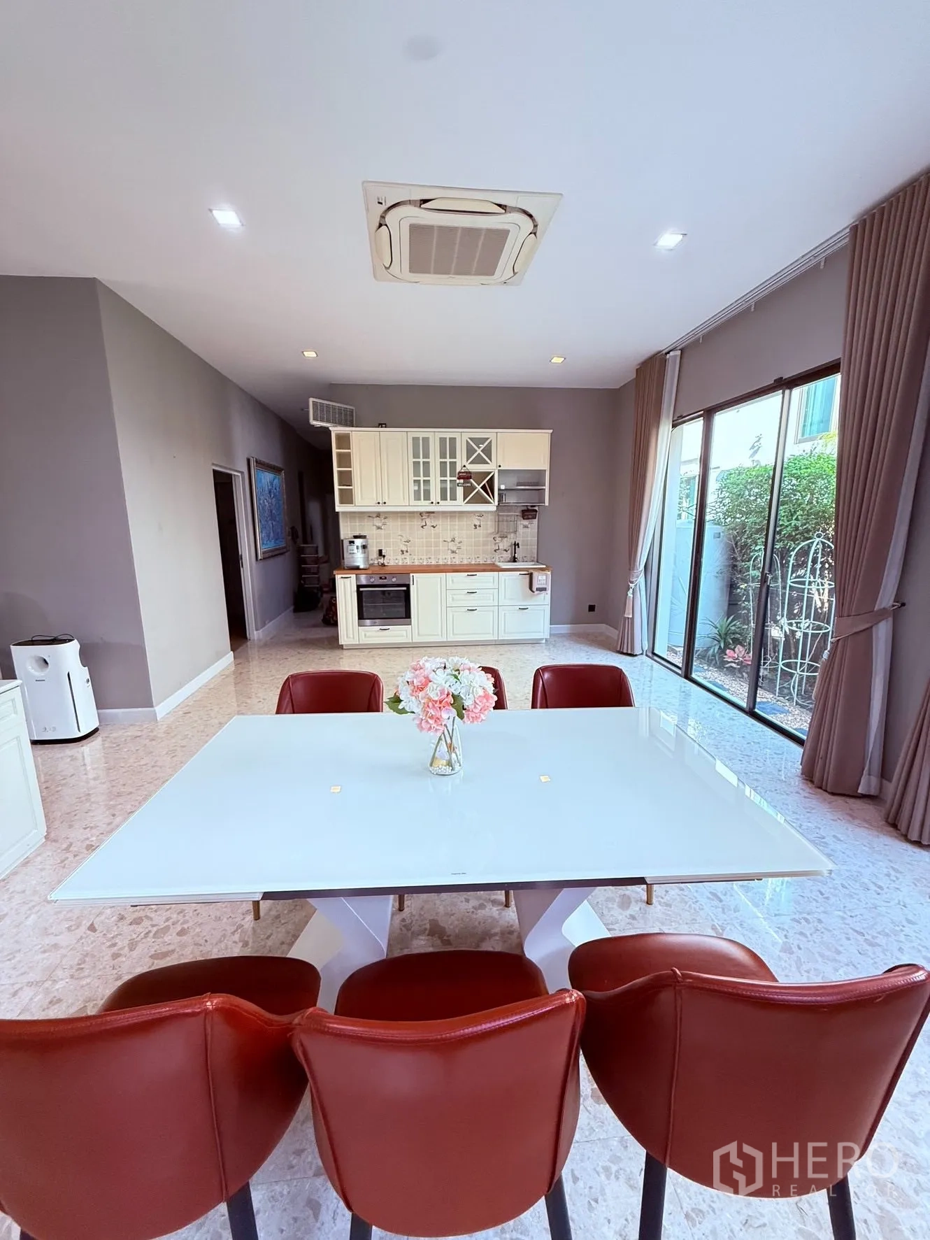 Detached House for rent or sale in Prawet, Bangkok - Dining area with white table and red chairs beside an open kitchenette and sliding glass doors.