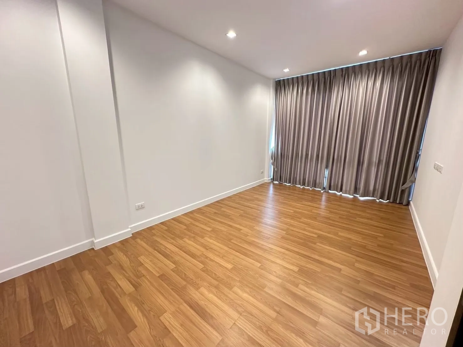 Home Office for rent in Lat Phrao, Bangkok - Cozy room with wood floor and full-length blackout curtains on a large window.