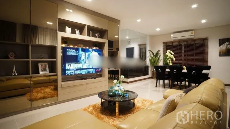Detached House for rent or sale in Bang Phli, Samut Prakan - Open-plan living room with built-in TV wall, leather sofa and recessed ceiling lights.