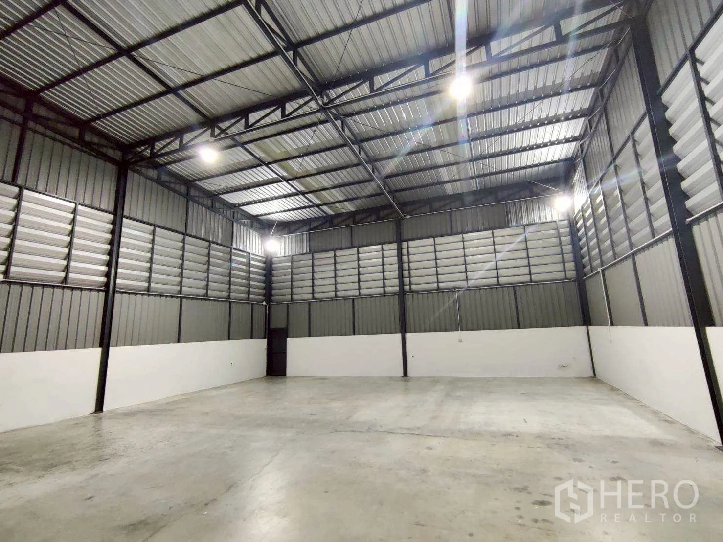Warehouse for rent in Lam Luk Ka, Pathum Thani - Empty storage space with high ceilings, ventilated metal wall panels, and LED lighting.