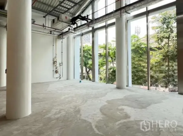 零售空间 出租在Phaya Thai, Bangkok - 采光充足的毛坯零售空间，落地窗、白色立柱、外露机电管线与水泥地面，面向街道绿化。