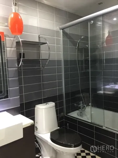 Condominium for rent in Watthana, Bangkok - Contemporary bathroom with gray tiles, glass shower over bathtub, vanity and orange pendant light.