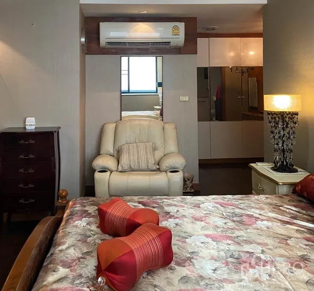 Condominium for rent in Khlong Toei, Bangkok - Cozy bedroom nook with recliner chair, mirrored wardrobe and bedside lamp.