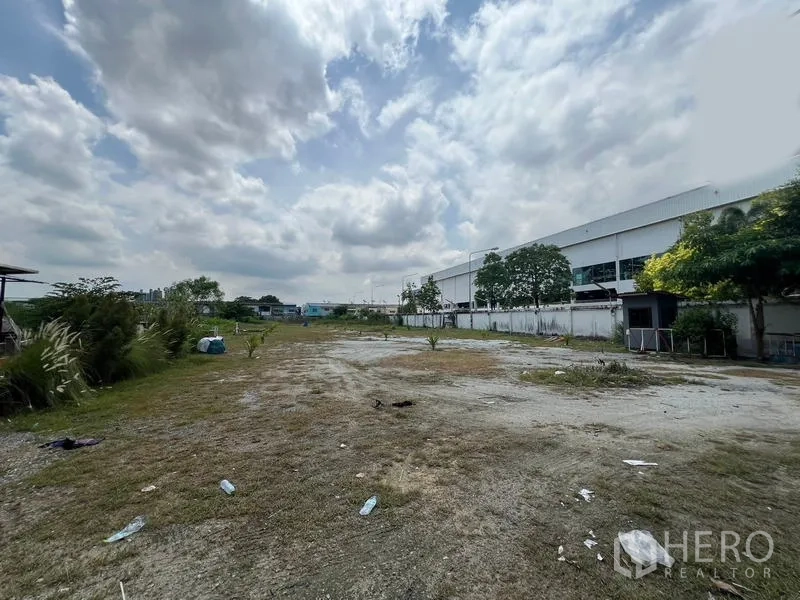 Showroom for rent in Mueang Samut Prakan, Samut Prakan - Spacious rear yard with gravel and grass beside neighboring industrial buildings