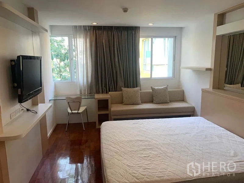 Condominium for rent or sale in Khlong Toei, Bangkok - Bright bedroom with two windows, sofa, desk, and TV.
