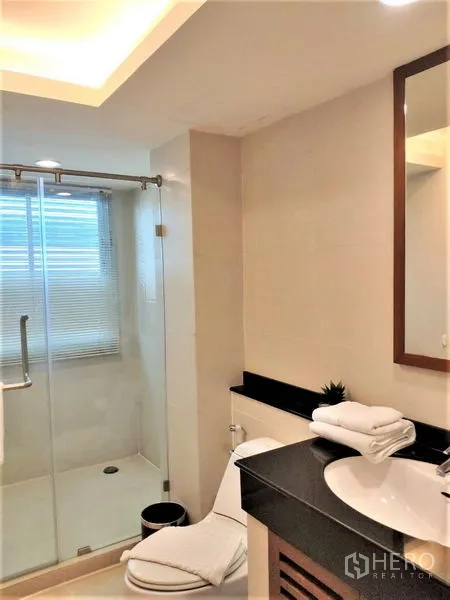Condominium for rent in Bang Rak, Bangkok - Modern bathroom with glass-enclosed shower, vanity and toilet.