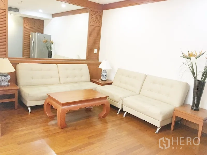 公寓 出租在Pathum Wan, Bangkok - 客厅配米色沙发、木质茶几与边几，墙面大型镜子。