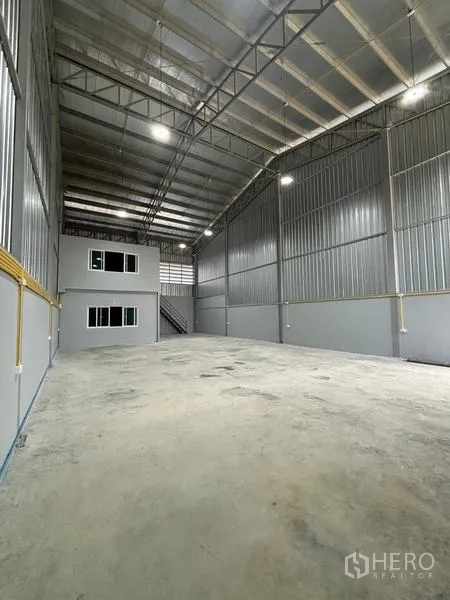 Warehouse for rent in Mueang Pathum Thani, Pathum Thani - Long interior view toward the office block, showing tall steel walls and LED lighting.