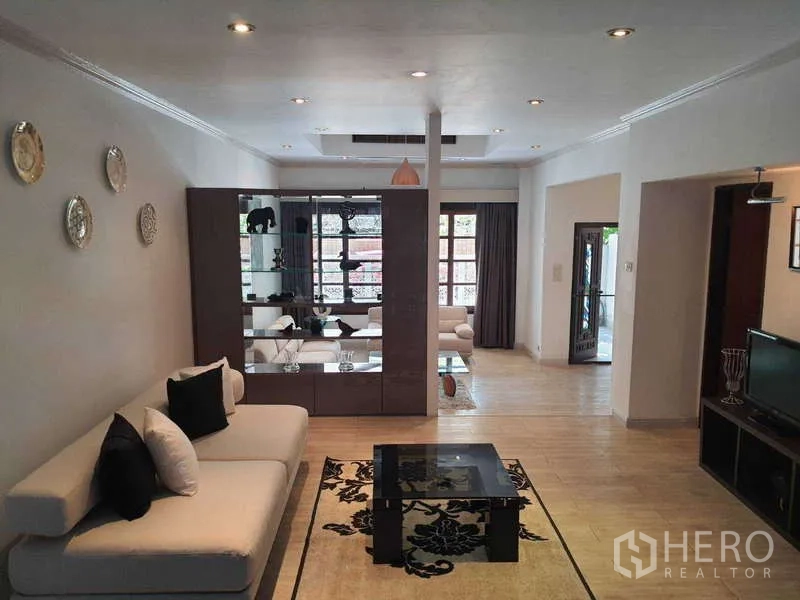 Townhouse for rent in Khlong Toei, Bangkok - Open-plan living room with partition display cabinet, neutral sofas and recessed lighting.
