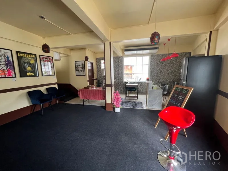 Shophouse for rent in Khlong Toei, Bangkok - Open living area beside a kitchenette with seating zones and a red bar stool under decorative lights.
