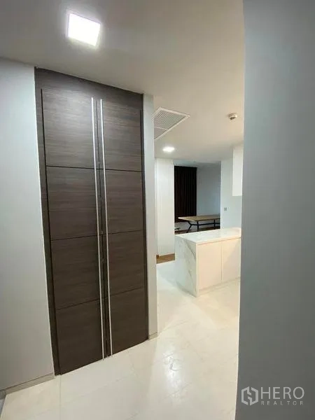 Condominium for rent or sale in Khlong Toei, Bangkok - Entry hallway with tall dark-wood storage and view to a white marble peninsula kitchen.