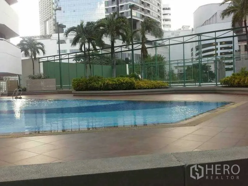 Condominium for rent in Watthana, Bangkok - Outdoor swimming pool with city buildings and palm trees around.