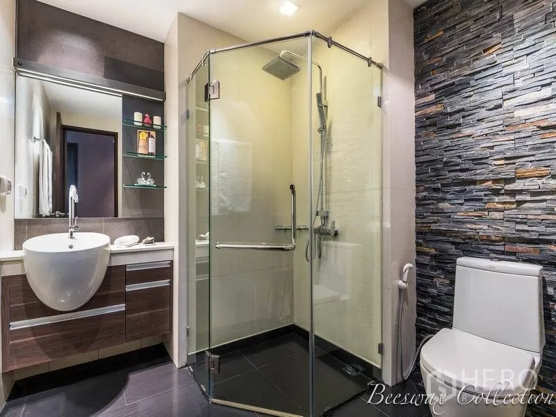 Condominium for rent in Watthana, Bangkok - Stylish bathroom with frameless glass shower, stone accent wall, wall‑hung vanity and toilet.