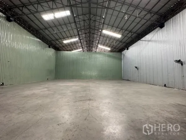 Warehouse for rent in Pak Kret, Nonthaburi - Open-plan warehouse highlighting tall ceiling, ribbed metal cladding and bright ceiling lights.